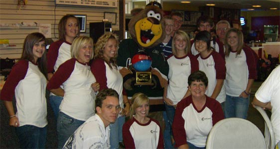 A large group of students pose with a large stuffed bear. 